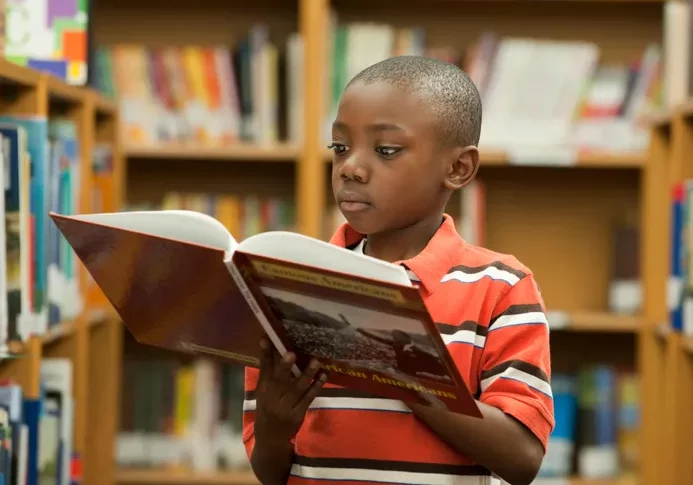 young black boy reading a book in a library